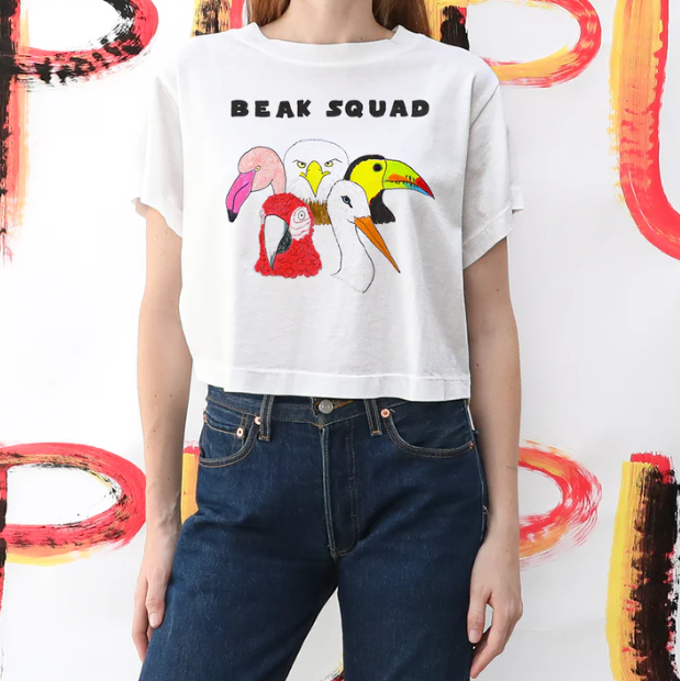 Person wearing a white t-shirt with 'BEAK SQUAD' and toucan graphics against a colorful abstract background.