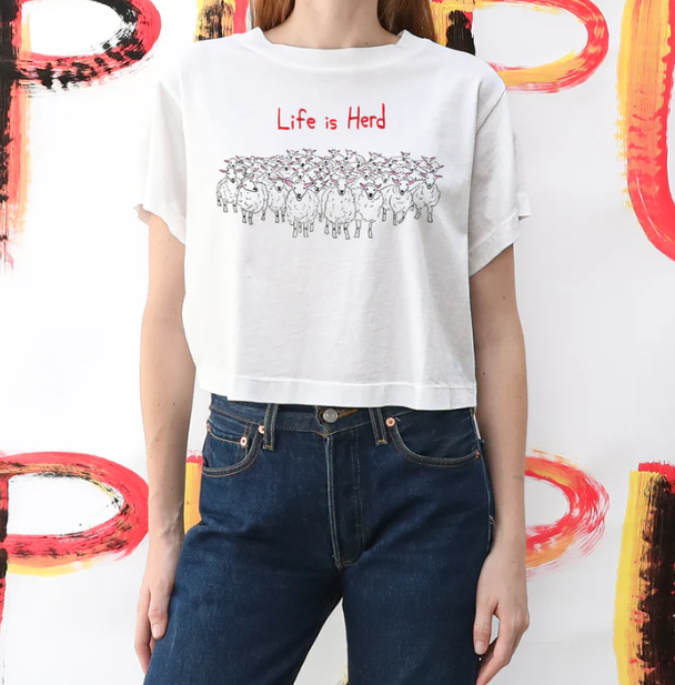 Person wearing a white t-shirt with 'Life is Hard' text and graphic design, standing against a colorful abstract background.