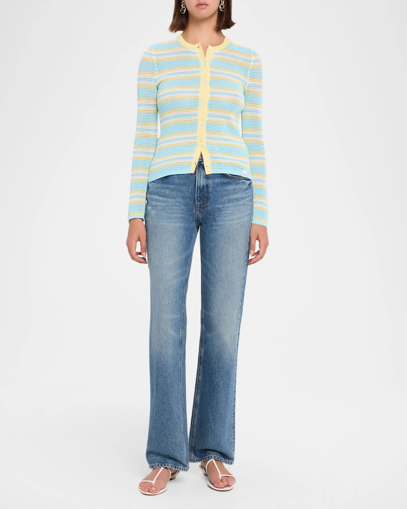 A model wearing a light blue and yellow striped knit cardigan with a yellow zipper, paired with blue jeans and pink sandals, against a plain white studio background.