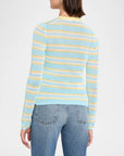 A woman shown from the back wearing a light blue knit sweater with horizontal yellow and white stripes, paired with blue jeans, against a plain white studio background.