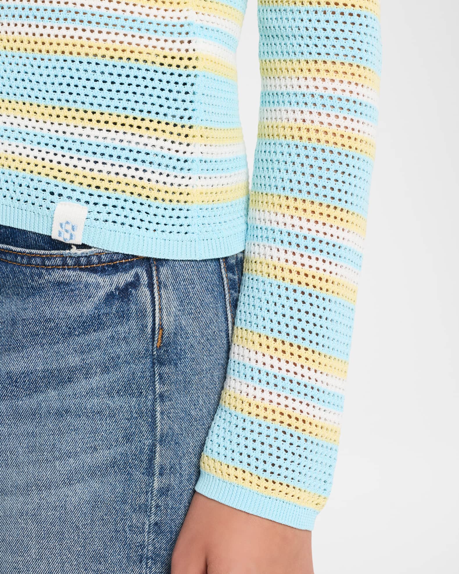 Close-up of a model wearing a light blue open-knit long-sleeve top with yellow and white horizontal stripes, paired with blue jeans.