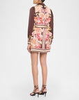 A model shown from the back wearing a brown satin jacket with a pink floral print and a matching belt, paired with black strappy heels against a light gray studio background.