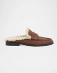 A brown suede slip-on loafer mule with a thick cream sherpa lining and a black sole, shown in profile against a light gray background.