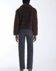 A model viewed from the back wearing a dark brown textured teddy-fur jacket, dark gray straight-leg jeans, and black high-heeled sandals against a plain white studio background.