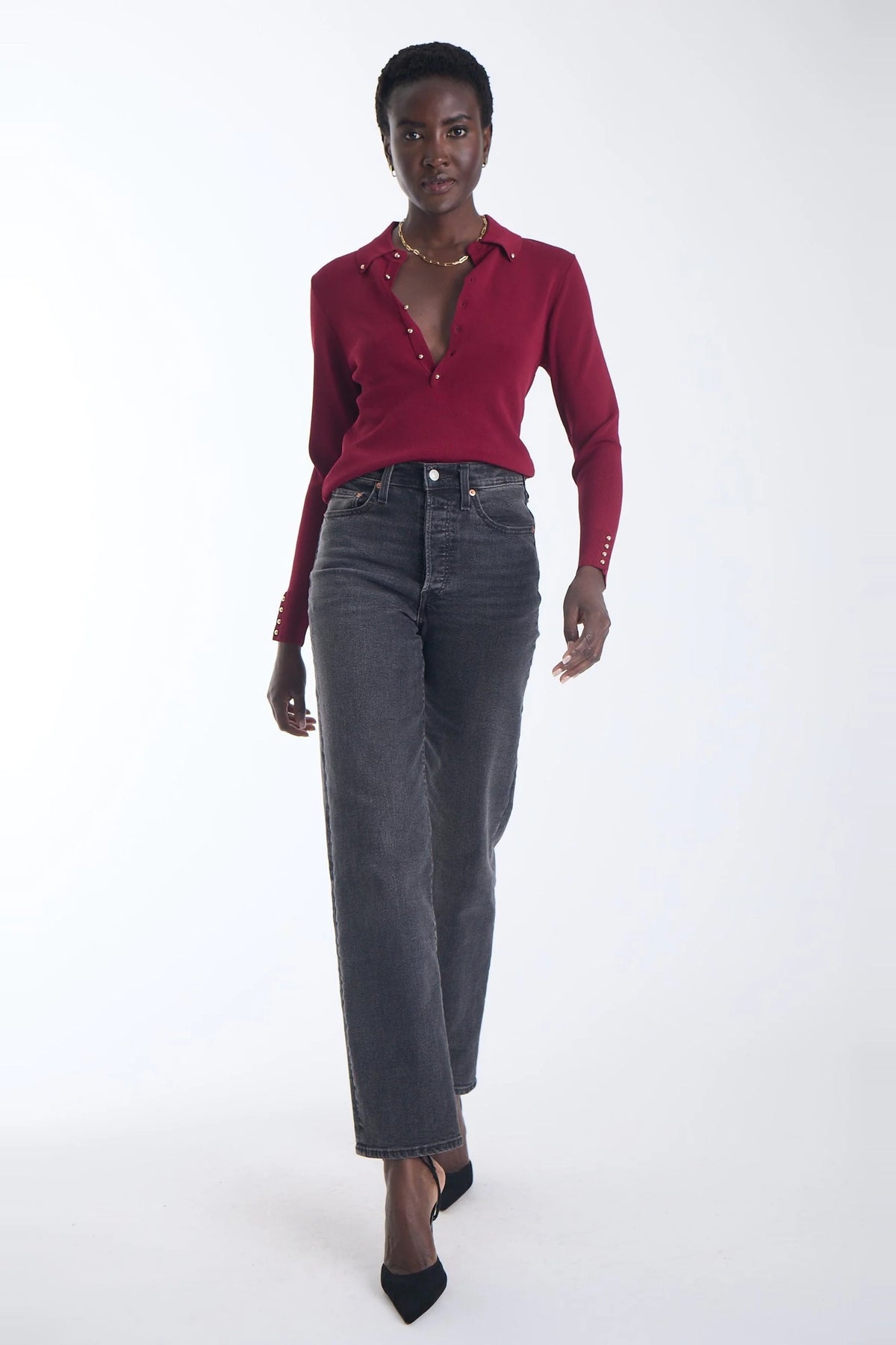 model wearing a wine colored top with gold stud details and grey jeans on a white background 
