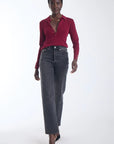 model wearing a wine colored top with gold stud details and grey jeans on a white background 