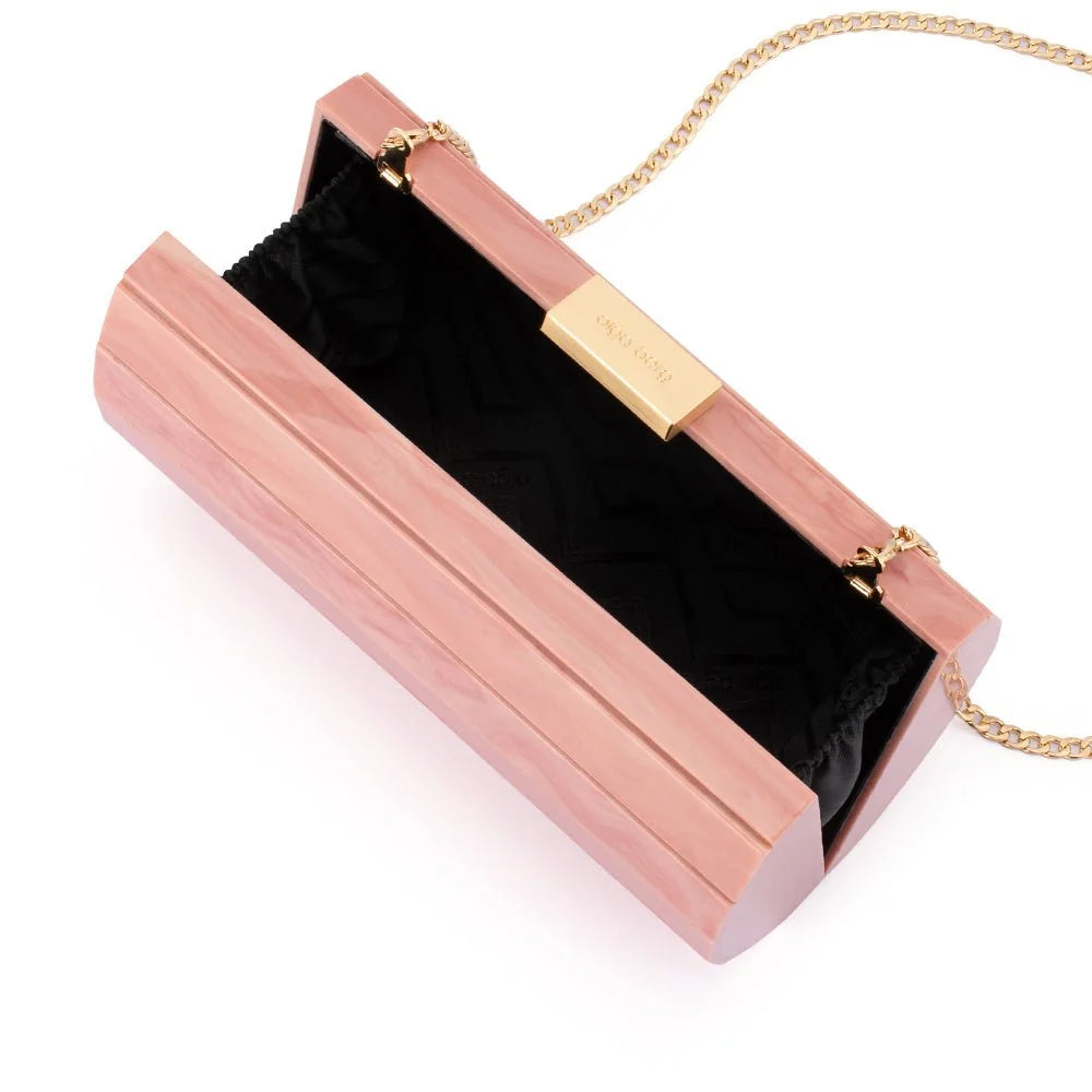 A rectangular clutch bag with a glossy pink wood-grain finish, featuring a black chevron-patterned interior lining and gold-tone hardware, including a gold clasp, a gold brand plaque, and a gold chain strap.
