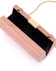 A rectangular clutch bag with a glossy pink wood-grain finish, featuring a black chevron-patterned interior lining and gold-tone hardware, including a gold clasp, a gold brand plaque, and a gold chain strap.