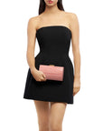 A woman wearing a strapless black mini dress and holding a pink textured clutch bag against a plain white background.