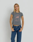 A blonde woman modeling a gray heather cropped t-shirt with a pink graphic of a horse and rider and the text 'PALM BEACH RIDING Club', paired with blue jeans, against a light gray studio background.