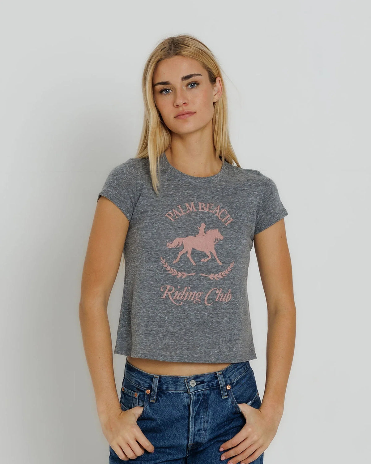 model wearing a grey tee with a pink graphic with jeans on a cream background 