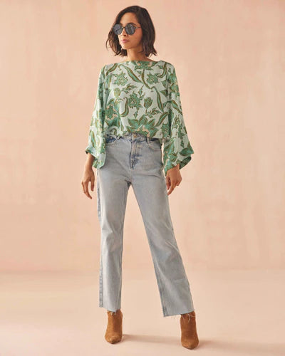 Woman wearing a green floral blouse, light blue jeans, and brown boots on a beige background