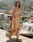 Woman in a patterned dress standing by a marina with boats in the background