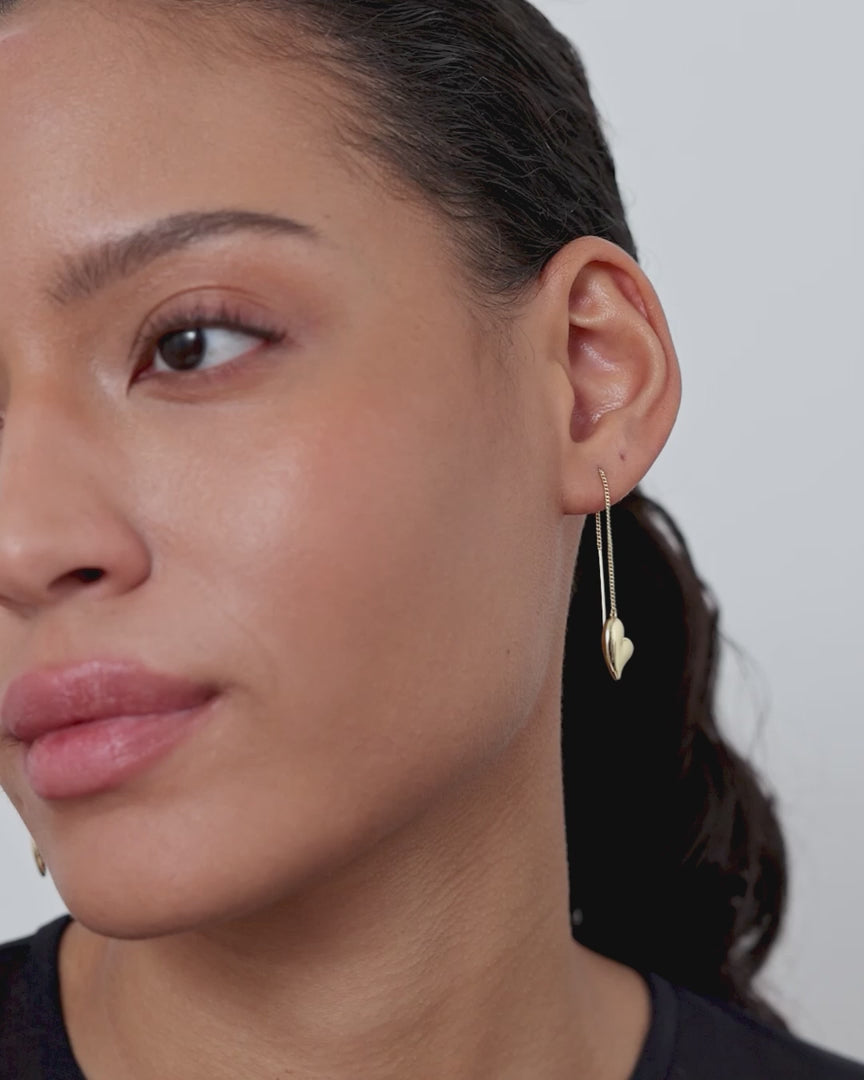 video of model wearing dangling gold heart earrings