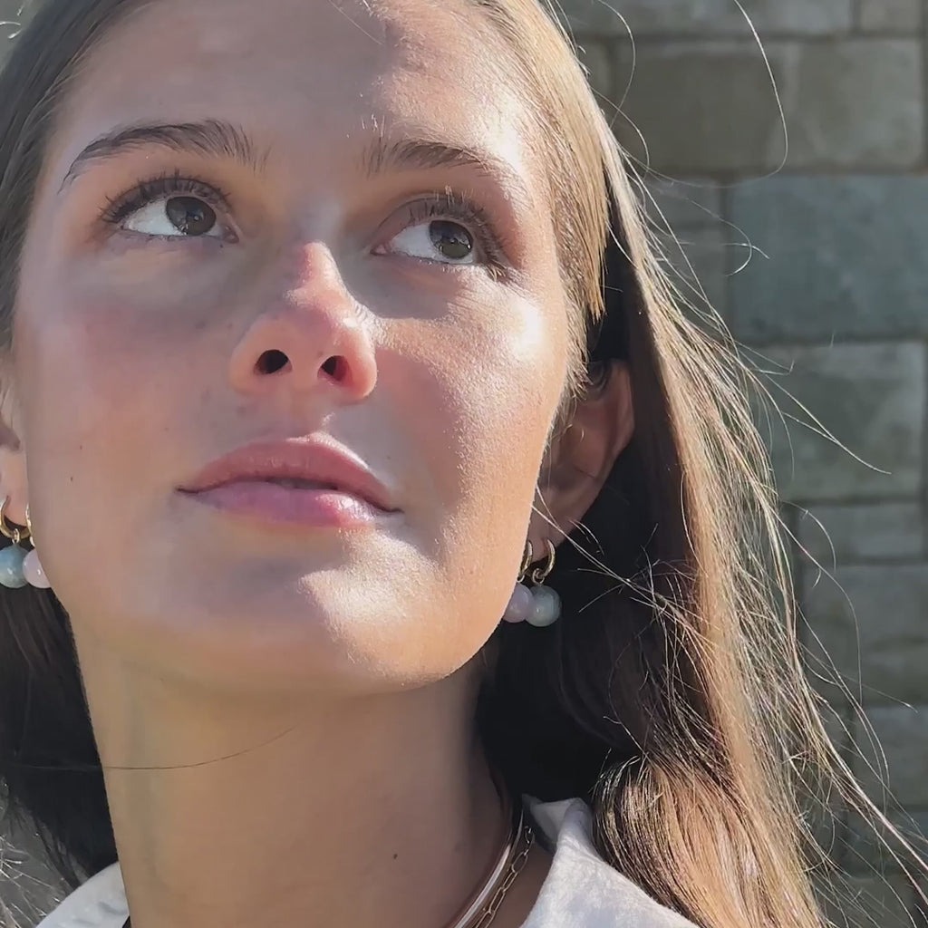 video of a woman wearing gold earrings with pink and aquamarine stones