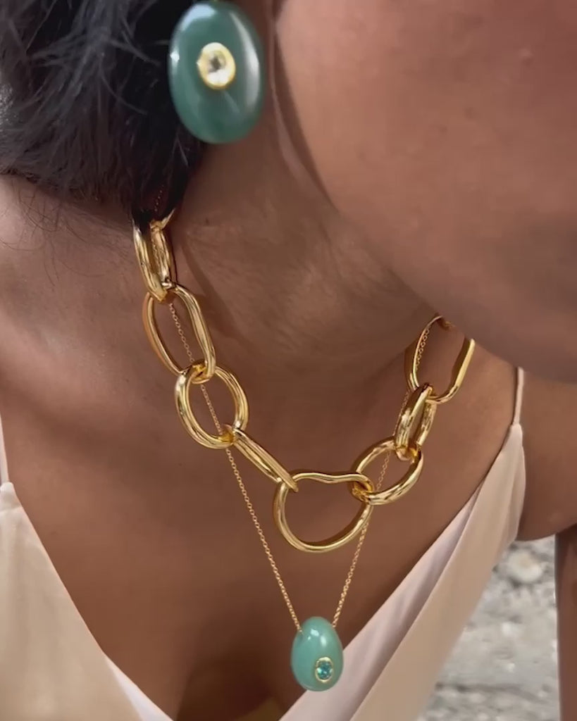 Video of a woman wearing gold chain earrings with a textured beige background