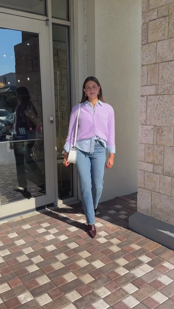 Model wearing purple sweater layered over button up with jeans, booties and Mccall Laser Cut Leather Saddle Bag. walking