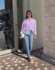 Model wearing purple sweater layered over button up with jeans, booties and Mccall Laser Cut Leather Saddle Bag. walking