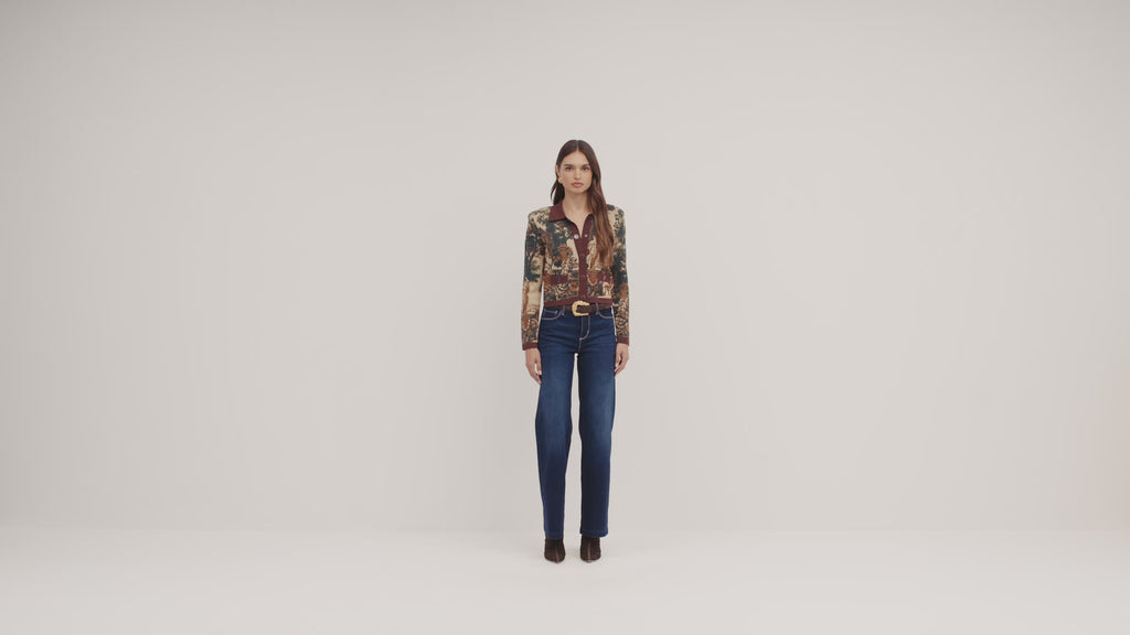 A model stands against a plain light background wearing a patterned long-sleeve blazer with a brown shirt and dark blue wide-leg jeans