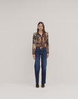 A model stands against a plain light background wearing a patterned long-sleeve blazer with a brown shirt and dark blue wide-leg jeans