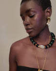 video of A model wearing a multi-strand necklace with white pearls, black beads, and gold-toned accents, along with matching gold hoop earrings and a gold pendant necklace, styled with a black strapless top against a light beige background.
