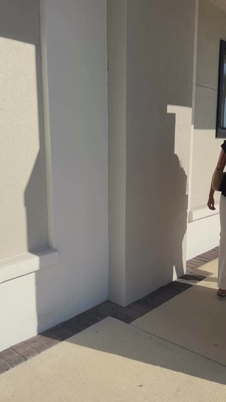 Model wearing Ganni top and white jeans with Clare V bag, walking