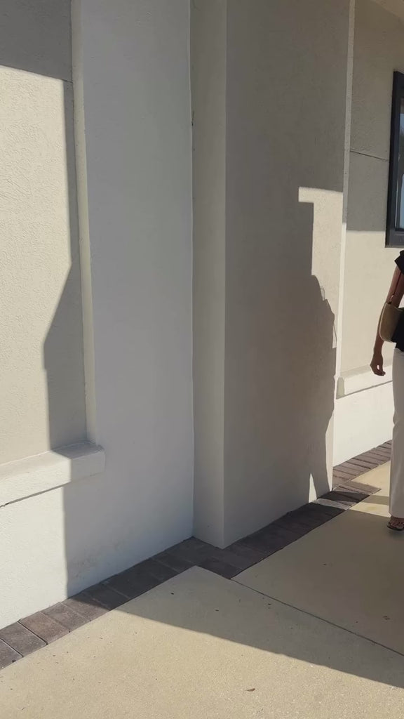 Model wearing Ganni top and white jeans with Clare V bag, walking