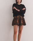 video of A woman standing in a studio wearing a black long-sleeve lace-trim top and a black shorts with a brown paisley pattern. 
