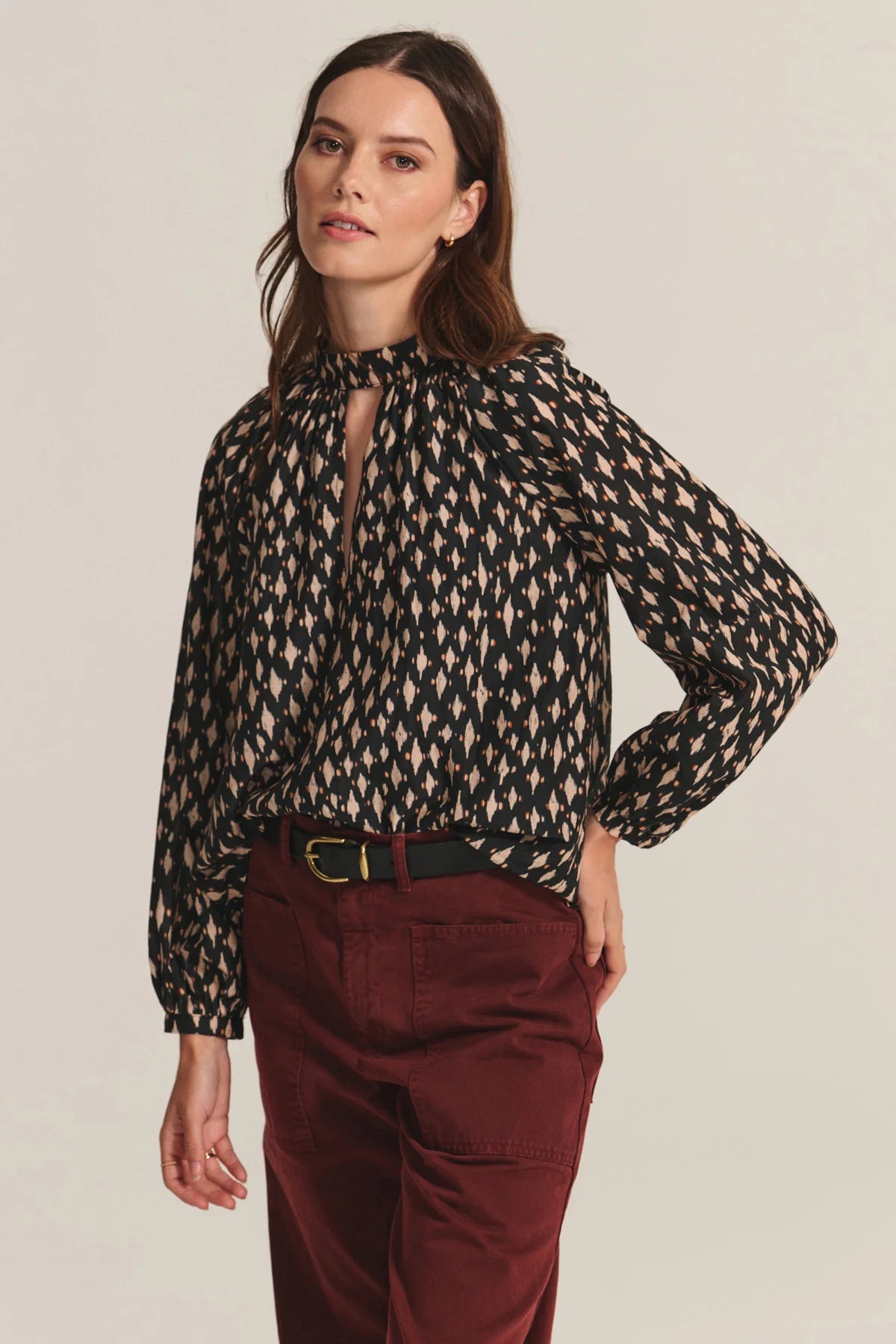 Woman wearing a patterned blouse and burgundy pants against a plain background