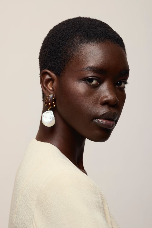 A close-up portrait of a model with short dark hair wearing a cream-colored top and Orbit Earrings in Pearl