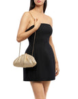 A woman wearing a strapless black mini dress and carrying a textured gold chain shoulder bag against a plain white background.