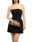A woman wearing a strapless black mini dress and holding a metallic gold clutch purse, shown against a plain white background.