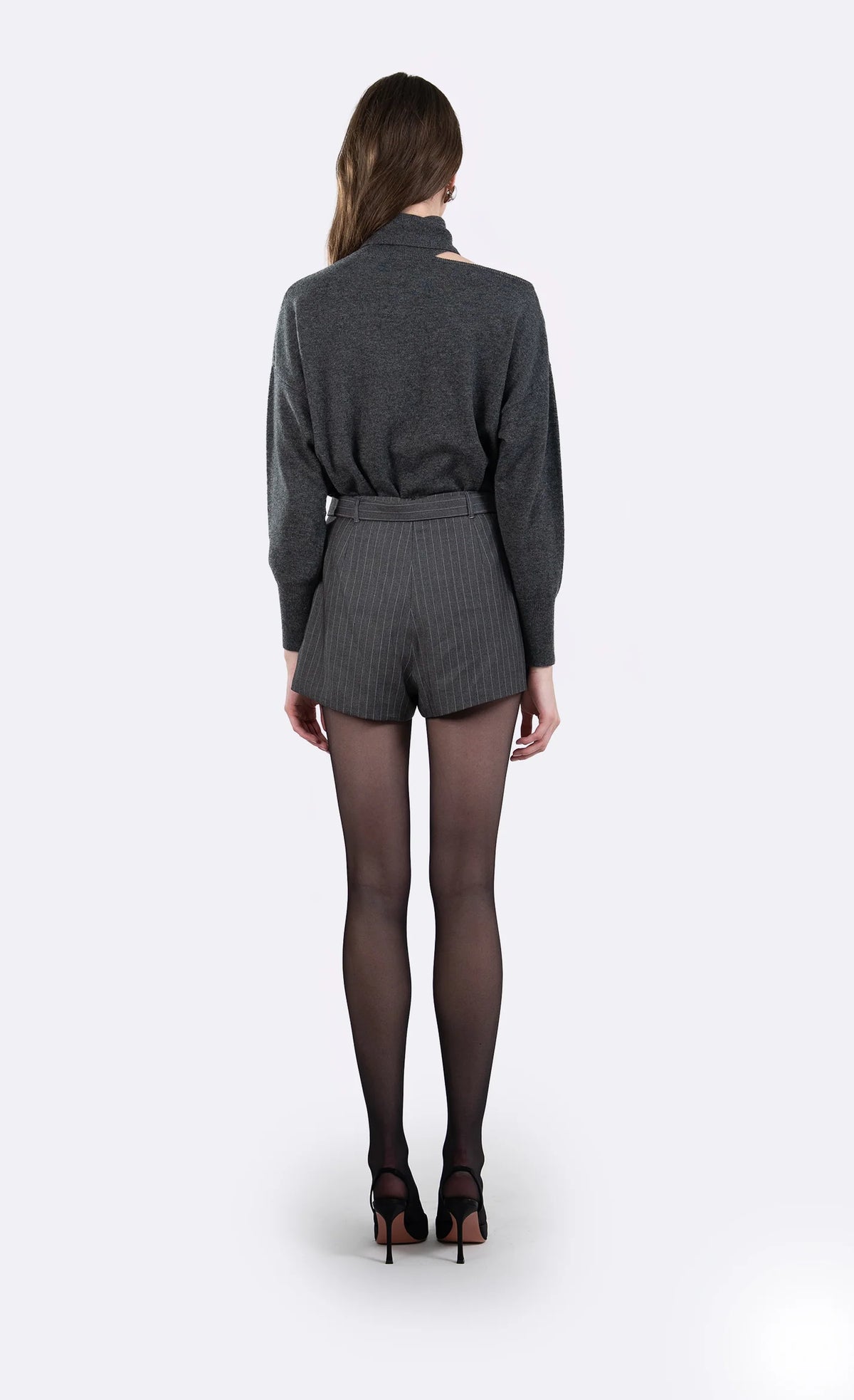 A model shown from the back wearing a dark gray ribbed long-sleeve top and matching gray pinstriped shorts, paired with sheer black tights and black high heels, against a light gray studio background.