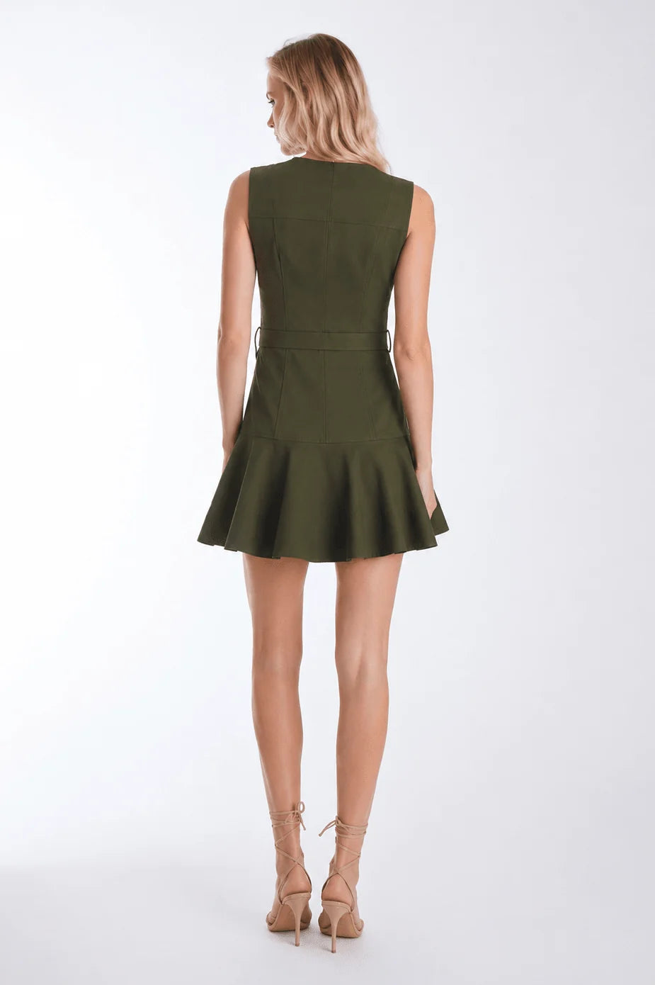 A woman shown from the back wearing a sleeveless olive green mini dress with a defined waist and flared skirt, paired with beige lace-up high heels, against a plain white studio background.