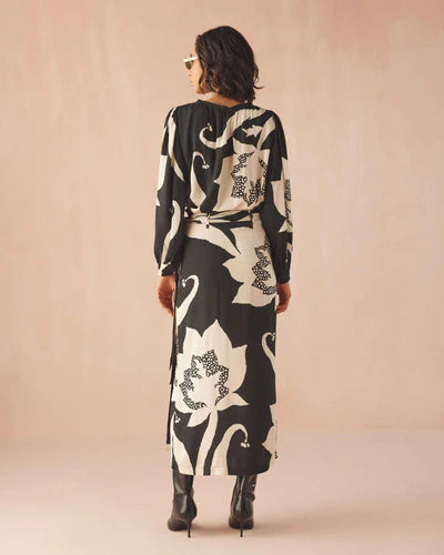 Woman wearing a long, black and white floral dress against a beige background