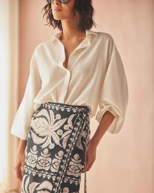 Woman wearing a white blouse and patterned black and white skirt against a light pink background, close up