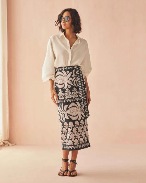 Woman wearing a white shirt and black patterned skirt against a pink background