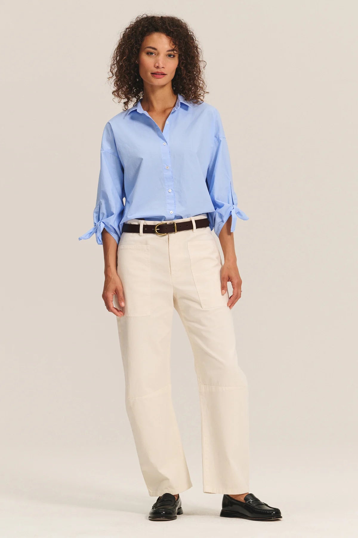 Woman wearing a light blue shirt and beige pants on a plain background