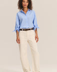 Woman wearing a light blue shirt and beige pants on a plain background