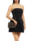 A woman modeling a black strapless mini dress and carrying a brown woven clutch with a thin gold chain strap against a plain white background.