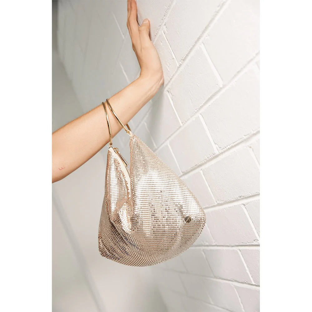Gold mesh handbag held by a hand against a light tiled wall.