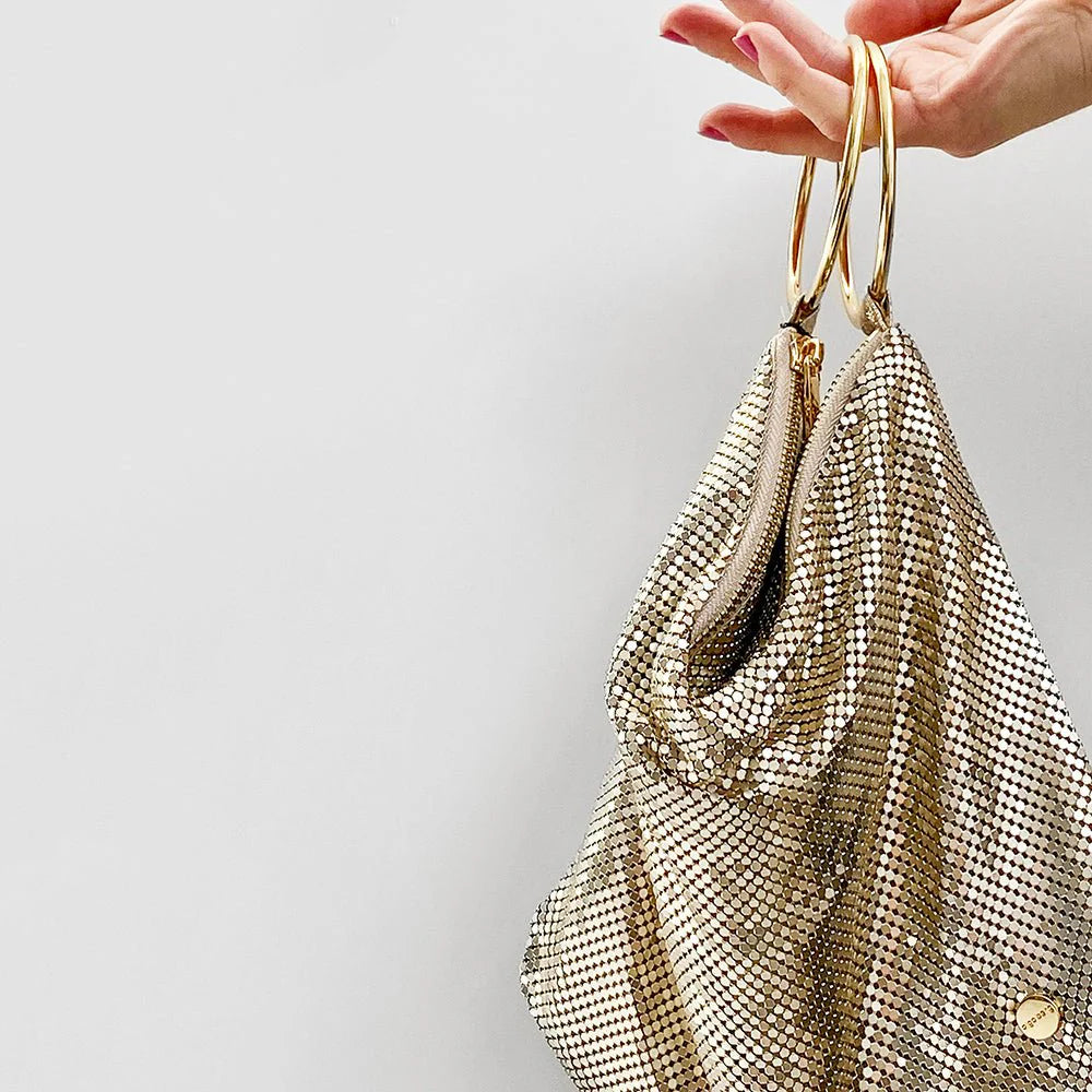 Gold mesh handbag held by a hand against a light gray background