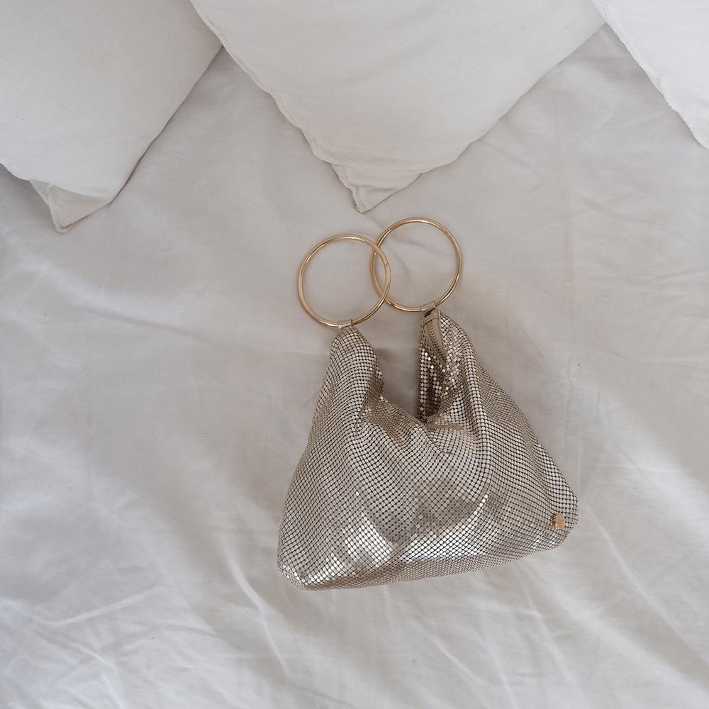 Metallic mesh bag with gold rings on a white fabric background