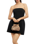 A woman wearing a strapless black mini dress and holding a small, textured metallic gold handbag against a plain white background.