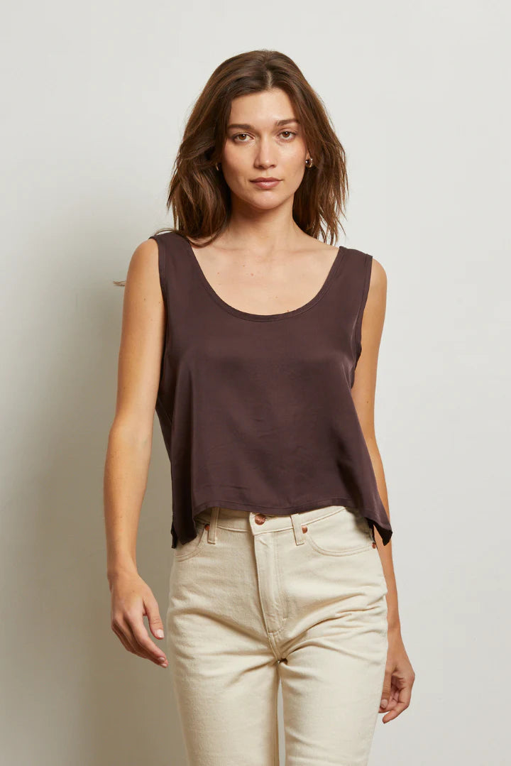 Woman wearing a brown sleeveless top and beige pants against a plain background front view