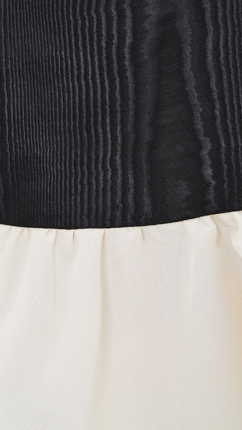 Close-up of a garment showing a black vertically textured upper section and an off-white lower section.