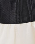 Close-up of a garment showing a black vertically textured upper section and an off-white lower section.