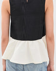 A woman shown from the back wearing a sleeveless color-block top with a black upper section and an off-white peplum lower section, paired with light blue jeans against a light gray studio background.