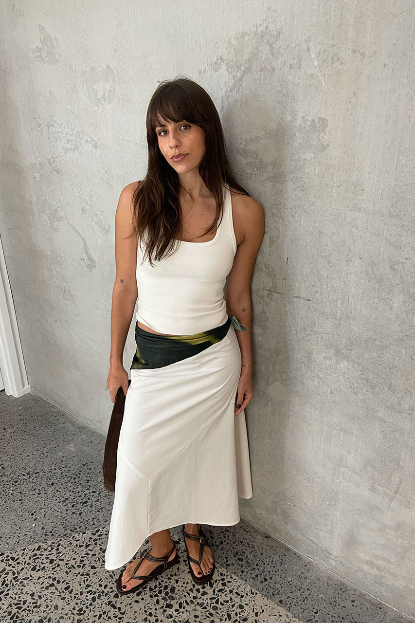 Woman wearing a white sleeveless top and skirt against a gray wall.