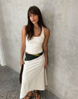 Woman wearing a white sleeveless top and skirt against a gray wall.